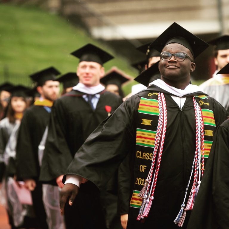 Proud male student in glasses leading a line of graduates in cap and gown