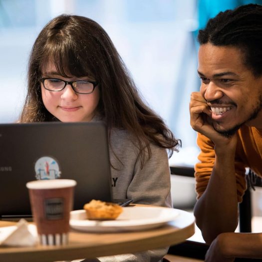 Female student on a computer being taught by a male teacher who is on her left